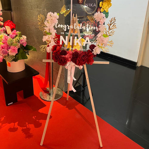 A floral congratulations sign on a wooden easel, decorated with red, pink, and white flowers, butterflies, and paper flowers - suitable for grand openings